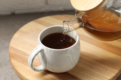 Photo of Pouring aromatic tea in cup at table, closeup