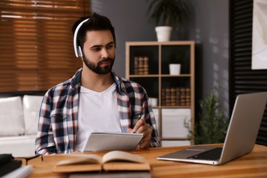 Photo of Young man watching webinar at table in room