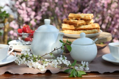 Photo of Beautiful spring flowers, freshly baked waffles and ripe strawberries on table served for tea drinking in garden