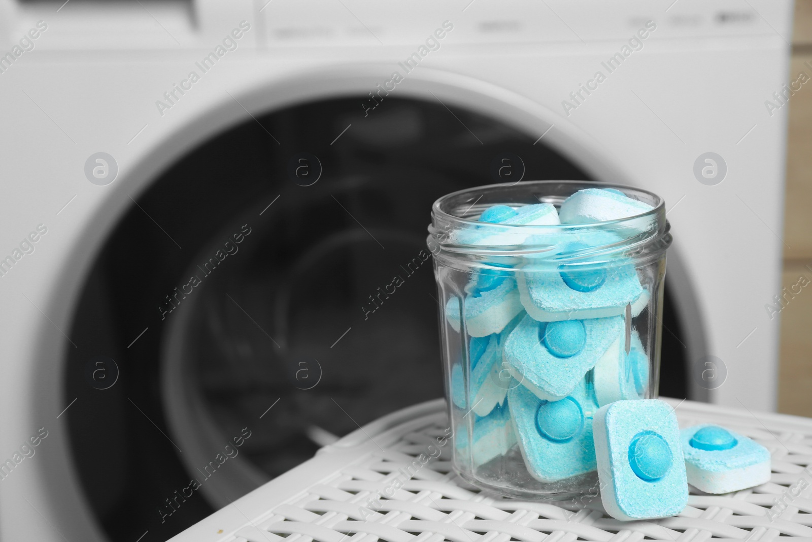 Photo of Jar with water softener tablets on laundry basket near washing machine, space for text