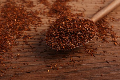 Photo of Spoon with dry rooibos leaves on wooden table, closeup. Space for text
