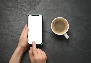 Photo of MYKOLAIV, UKRAINE - JULY 8, 2020: Woman using Iphone 11 Pro Max with blank screen and cup of coffee on black background, top view