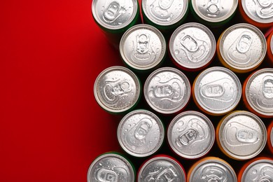 Photo of Energy drinks in wet cans on red background, top view. Space for text