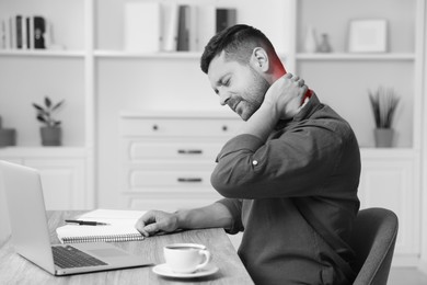 Image of Man suffering from neck pain at table, black and white effect