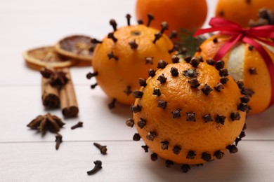 Photo of Pomander balls made of tangerines with cloves on white wooden table, closeup