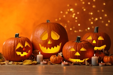 Photo of Pumpkin jack o'lanterns, autumn leaves and candles on table against blurred background. Halloween decor