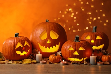 Photo of Pumpkin jack o'lanterns, autumn leaves and candles on table against blurred background. Halloween decor