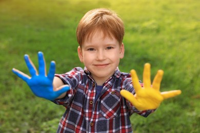 Photo of Little boy with hands painted in Ukrainian flag colors outdoors. Love Ukraine concept