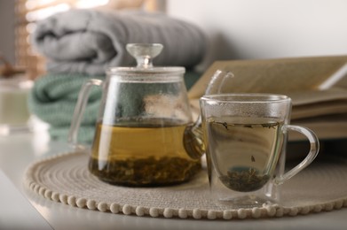 Photo of Glass teapot and cup of hot tea on table in room. Cozy home atmosphere