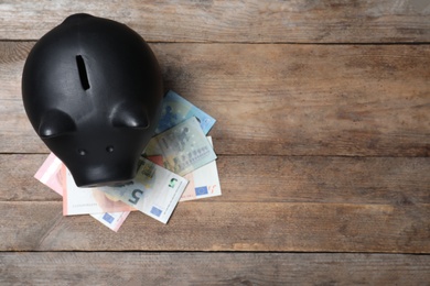 Photo of Top view of piggy bank and Euro banknotes on wooden table, space for text. Money savings