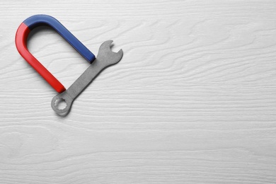 Photo of Magnet attracting wrench on light wooden background, flat lay. Space for text