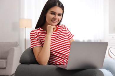 Photo of Happy young woman having video chat via laptop on sofa in living room