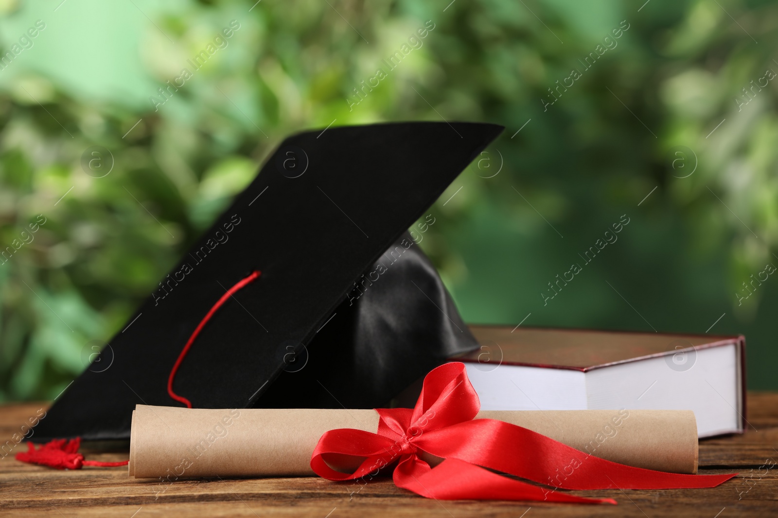 Graduation hat, book and diploma on wooden table against blurred background Photo of Graduation hat, book and diploma on wooden table against blurred background