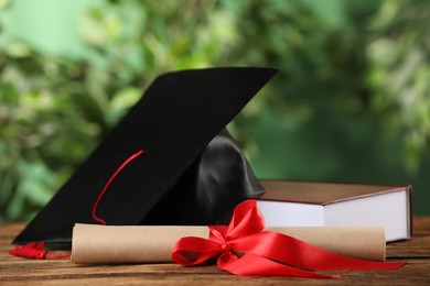 Photo of Graduation hat, book and diploma on wooden table against blurred background