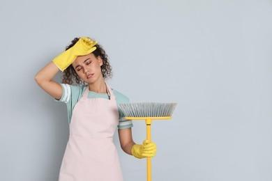 Photo of Tired African American woman with yellow broom on grey background, space for text