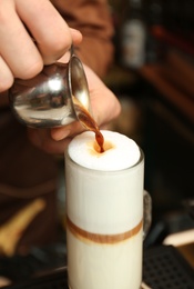 Photo of Barista adding coffee to steamed milk at counter, closeup view