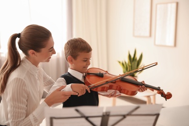Photo of Young woman teaching little boy to play violin indoors