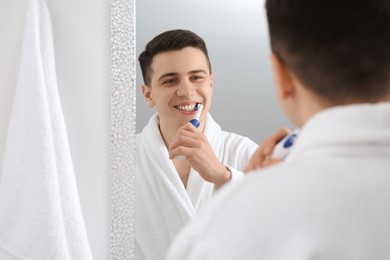 Photo of Man brushing his teeth with electric toothbrush near mirror in bathroom