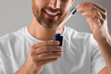 Photo of Man with cosmetic serum on light grey background, closeup