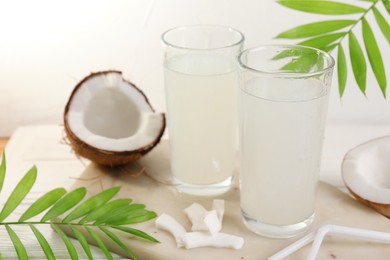 Photo of Glasses of coconut water, palm leaves and nuts on white table