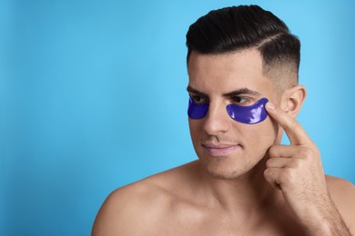Photo of Man applying under eye patch on light blue background. Space for text