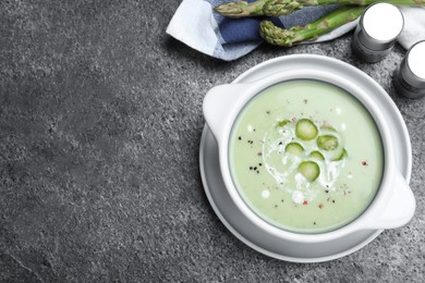 Photo of Bowl of delicious asparagus soup on grey table, flat lay. Space for text