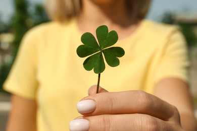 Photo of Woman holding green four leaf clover outdoors, closeup