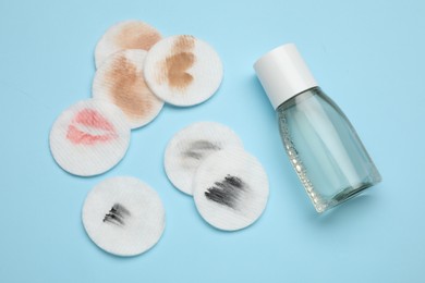 Photo of Bottle of makeup remover and dirty cotton pads on light blue background, flat lay