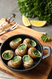 Photo of Delicious cooked snails in baking dish served on grey table, closeup