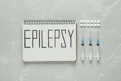 Photo of Notebook with word Epilepsy, pills and syringes on light grey table, flat lay