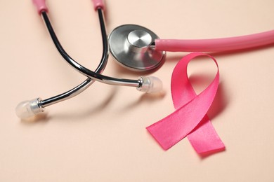 Pink ribbon and stethoscope on beige background, closeup. Breast cancer awareness