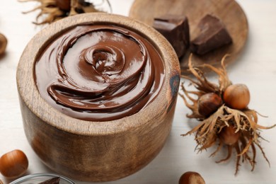 Photo of Bowl of tasty chocolate paste with hazelnuts on white wooden table
