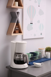 Photo of Modern coffeemaker and dishware on grey table in kitchen