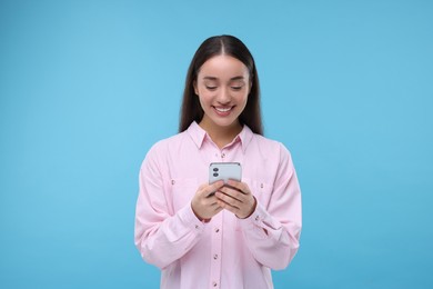 Photo of Happy woman sending message via smartphone on light blue background