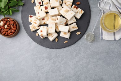 Photo of Pieces of delicious nutty nougat, peanuts and honey on light gray table, flat lay. Space for text