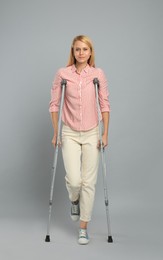 Photo of Young woman with axillary crutches on grey background