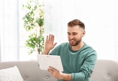Photo of Young man using video chat on tablet in living room