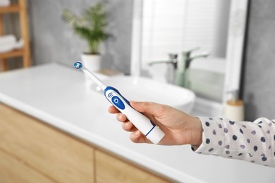 Photo of Woman holding electric toothbrush in bathroom at home, closeup