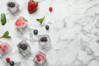 Photo of Ice cubes with different berries and mint on white marble table, flat lay. Space for text