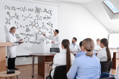 Image of Professors giving lecture in chemistry to audience in conference room. Projection screen with different illustrations