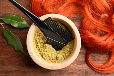 Photo of Bowl of henna powder, brush, green leaves and red strand on wooden table, flat lay. Natural hair coloring