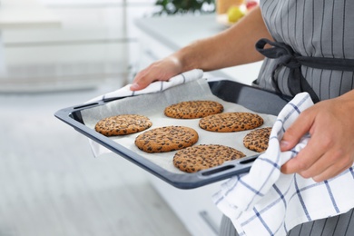 Photo of Young man holding oven sheet with cookies in kitchen, closeup