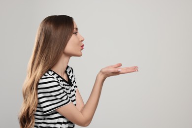 Photo of Beautiful young woman blowing kiss on light grey background. Space for text