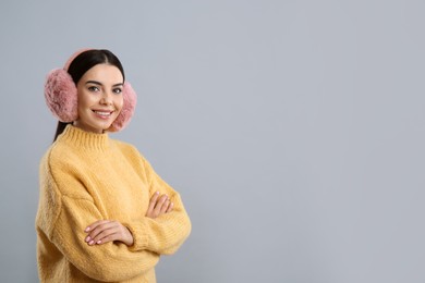Photo of Beautiful young woman wearing earmuffs on light grey background. Space for text