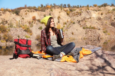 Photo of Female camper with thermos sitting on sleeping bag in wilderness