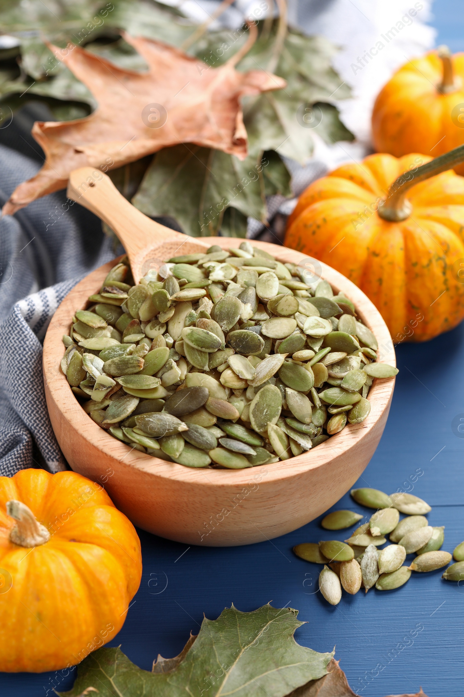 Bowl with seeds, fresh pumpkins and dry leaves on blue wooden table Photo of Bowl with seeds, fresh pumpkins and dry leaves on blue wooden table