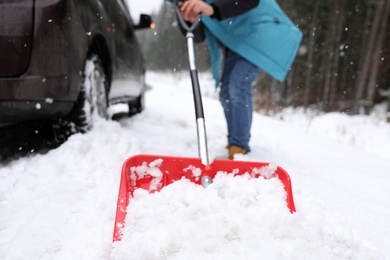 Photo of Man cleaning snow with shovel near stuck car outdoors
