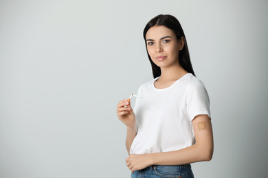 Photo of Young woman with nicotine patch and cigarette on light grey background. Space for text