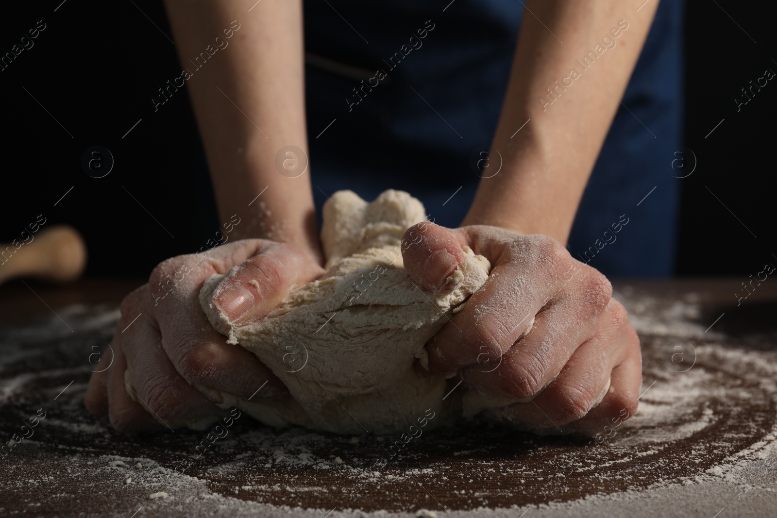 Photo of Making bread. Woman kneading dough at wooden table on dark background, closeup