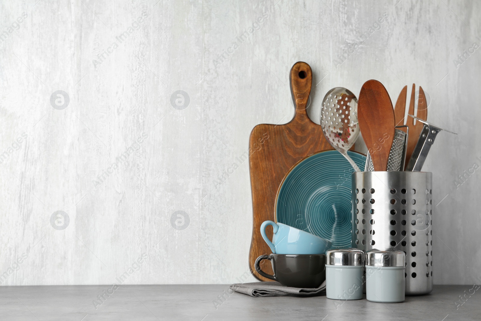 Photo of Different kitchen utensils on grey table against light background. Space for text